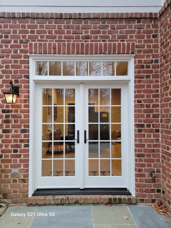 White double french patio doors with multi-pane transom set into a red brick wall.