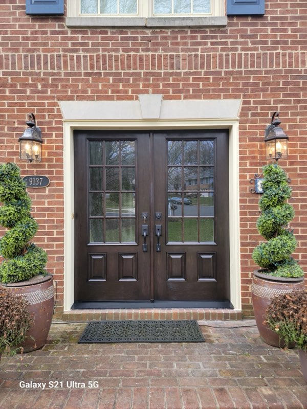Dark-stained wood double front entry doors with multi-pane glass tops set into a brick home with topiary planters.