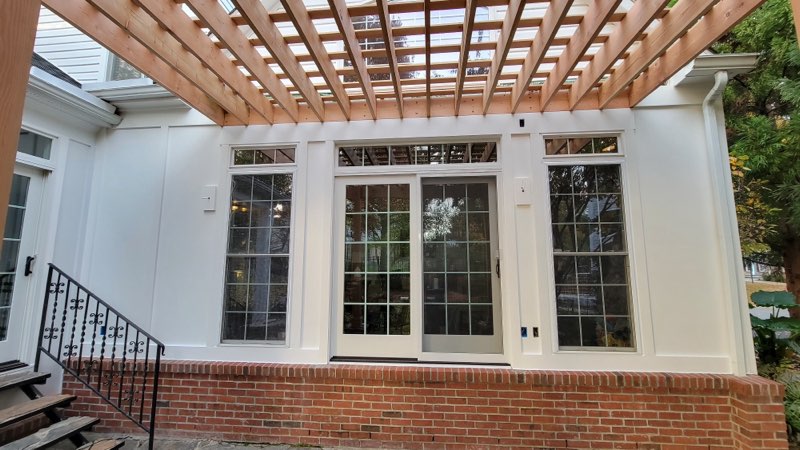 Sunroom addition with center french patio doors, flanking grid windows and transoms, under a cedar pergola.