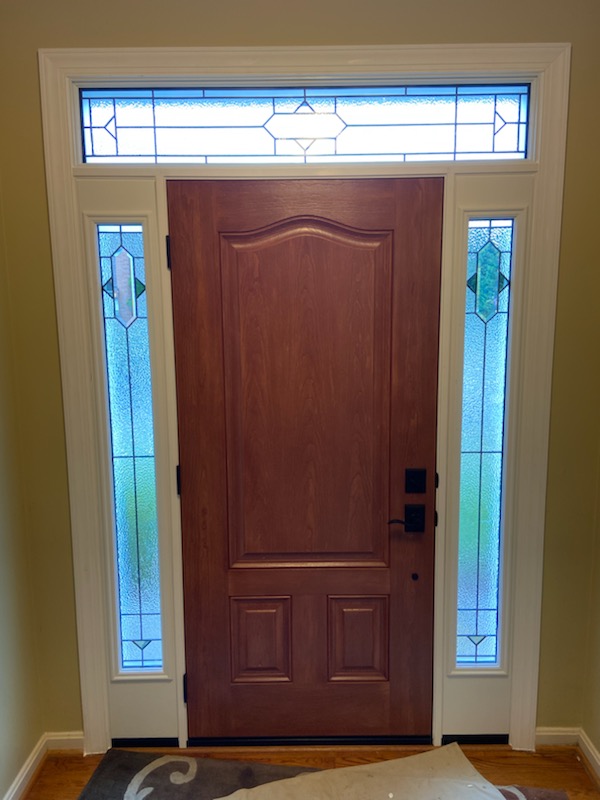 Stained wood front entry door with arched top panel, decorative leaded-glass sidelights, and transom, viewed from inside.