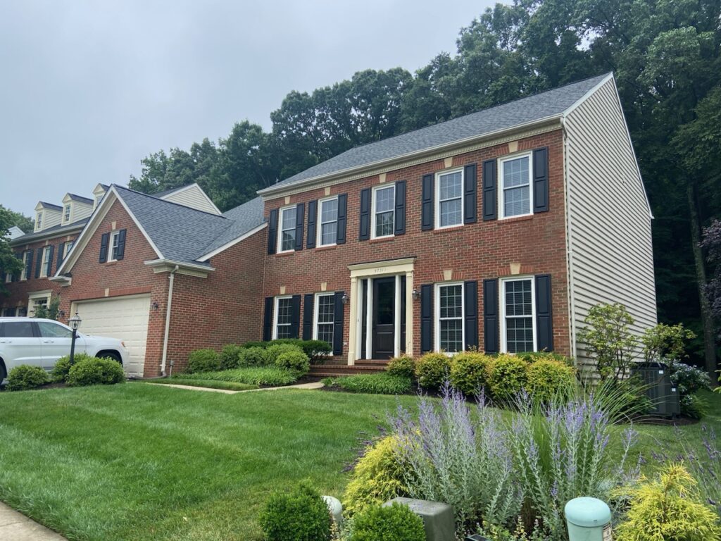 Brick colonial home with black-shuttered double-hung windows and architectural shingle roof.