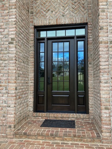 Black craftsman 6-lite front entry door with sidelights and transom set into a brick alcove with herringbone soffit.