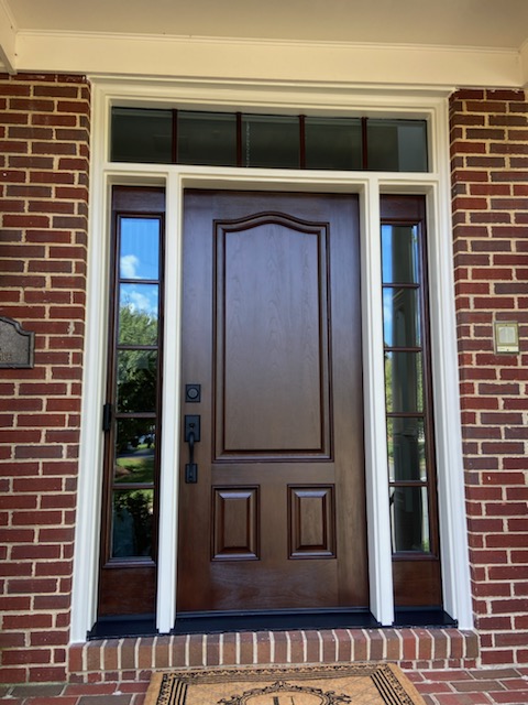 Stained wood front entry door with arched 3-panel design, multi-pane sidelights, and transom on a brick home.