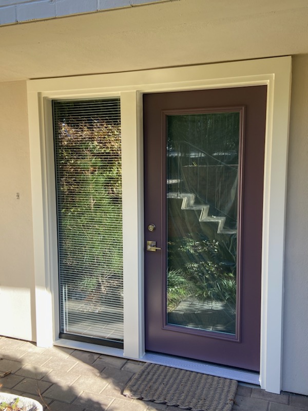 Burgundy full-glass rear entry door with a blind-shaded sidelight on a stucco wall.