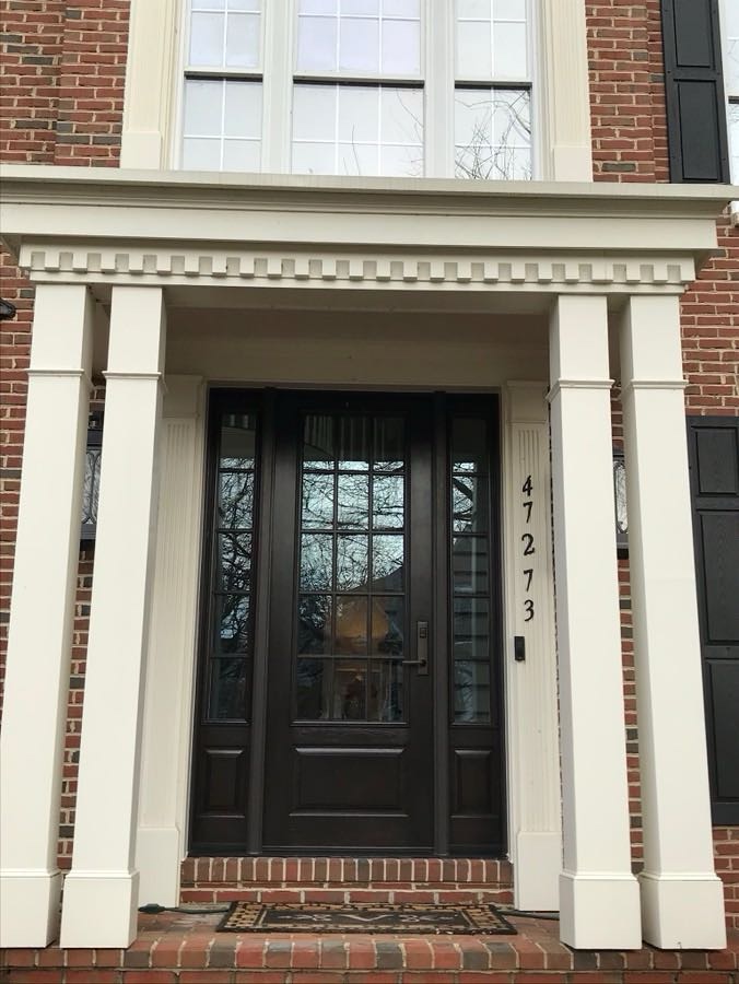 Dark wood front entry door with multi-pane glass top, sidelights, and white columned portico on a brick colonial, house number 47273.