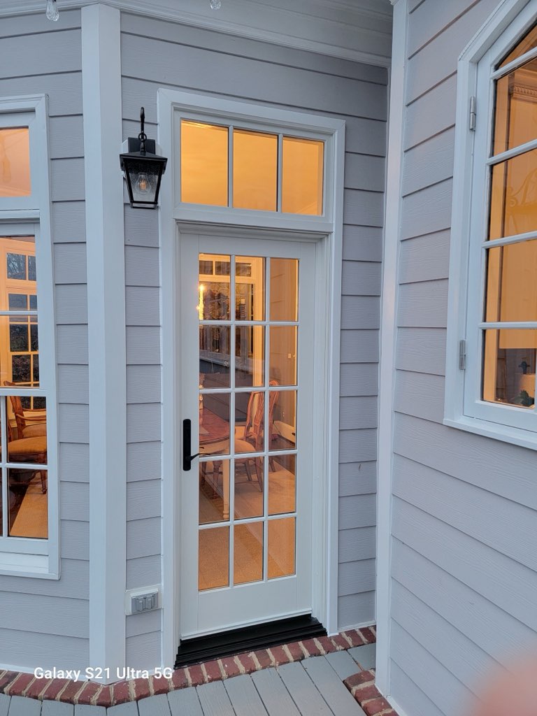 Single french door with transom and adjacent grid window on a gray lap-siding porch.