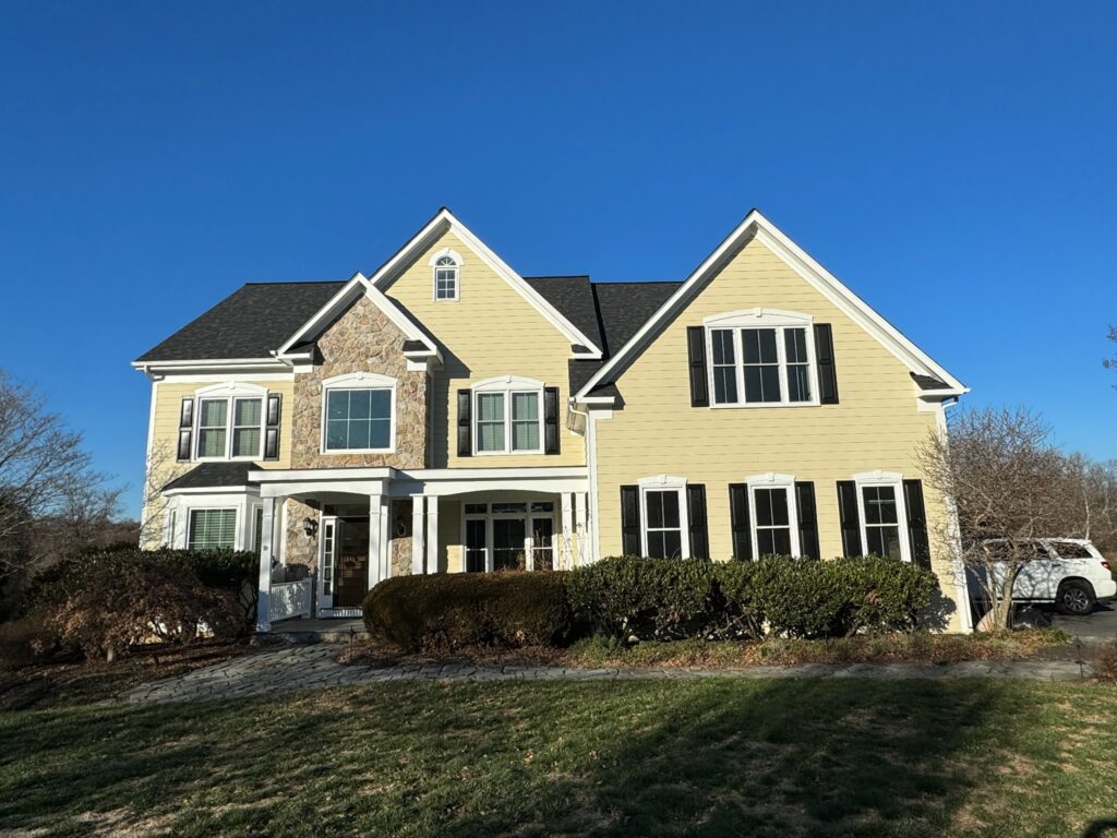 Two-story yellow lap siding home with stone front accent and white double-hung windows.