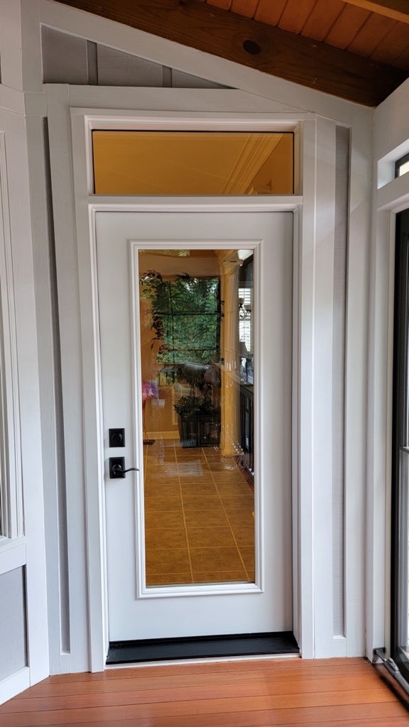 White glass-panel front entry door with transom under a covered porch.