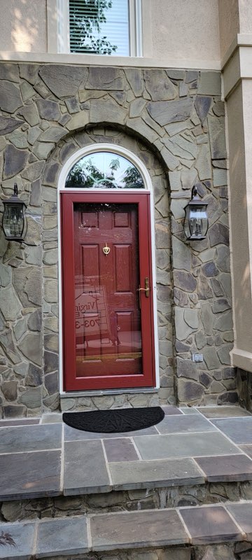 Red front entry door with arched stone surround and matching storm door.
