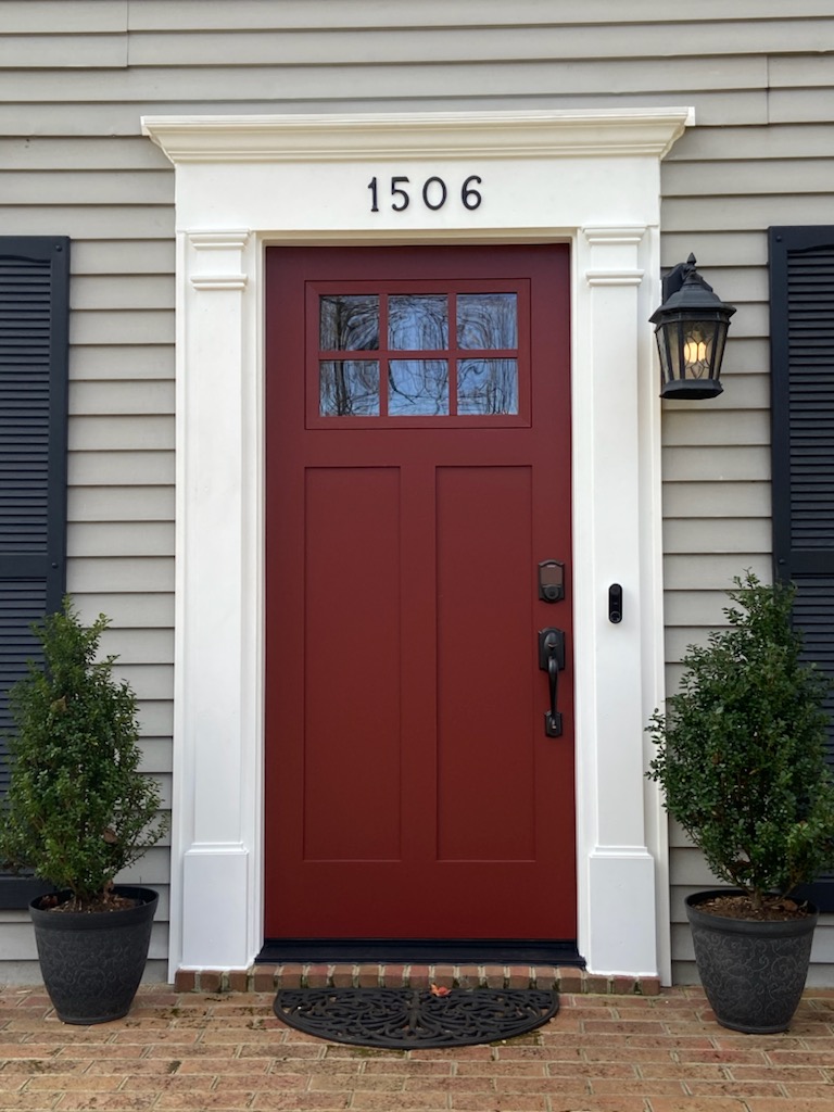Red craftsman front entry door with 6-lite glass and house number 1506 on gray lap siding.