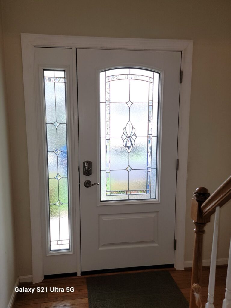White front entry door with decorative leaded-glass insert and matching sidelight, viewed from inside the foyer.