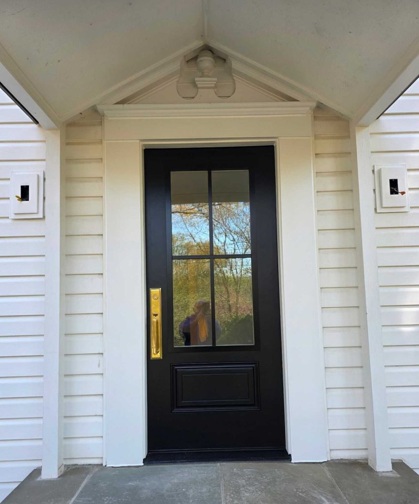 New black ProVia Smooth Fiberglass entry door with brass pull on a white-sided porch