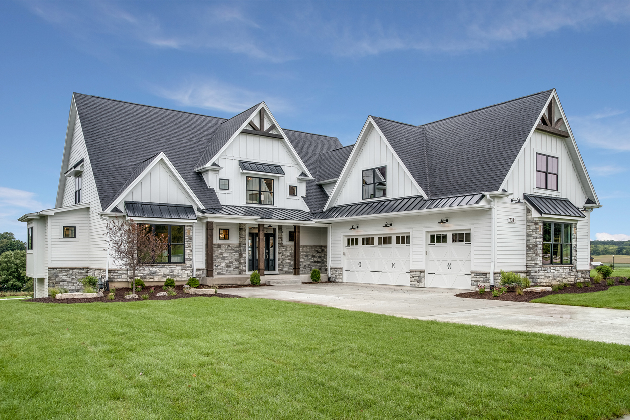 White modern farmhouse with black metal roof accents on open land