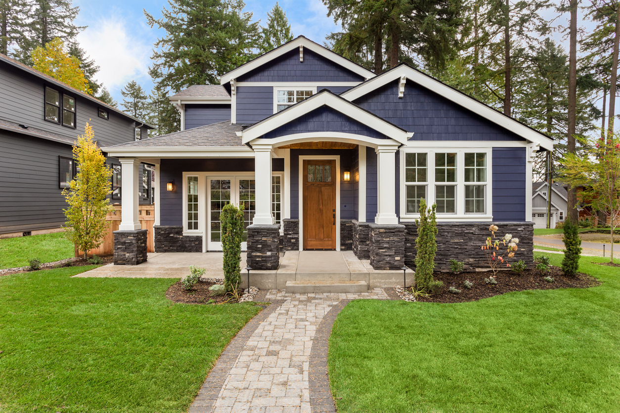Navy craftsman home with stone pillars among evergreens